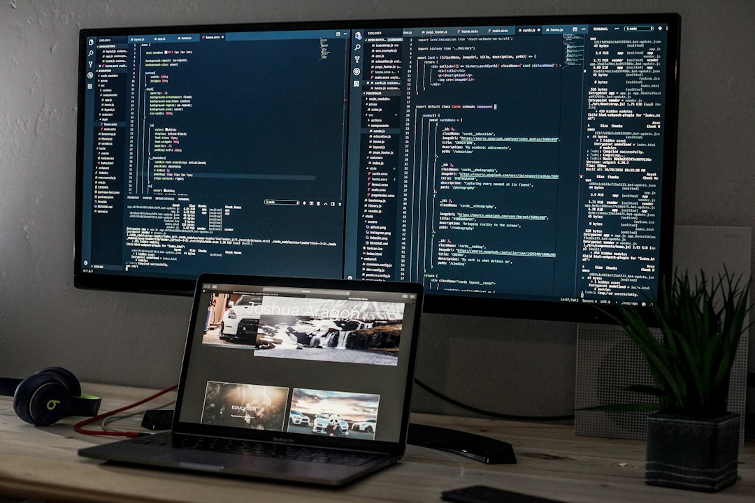 A laptop and a wide monitor displaying lines of code on a desk