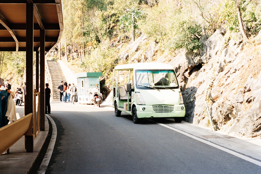 A small white shuttle bus drives on a paved road.