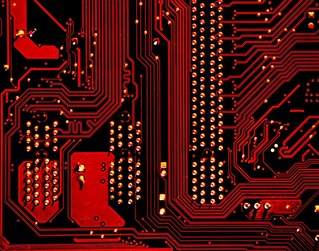 A red and black circuit board with intricate metallic pathways and solder points