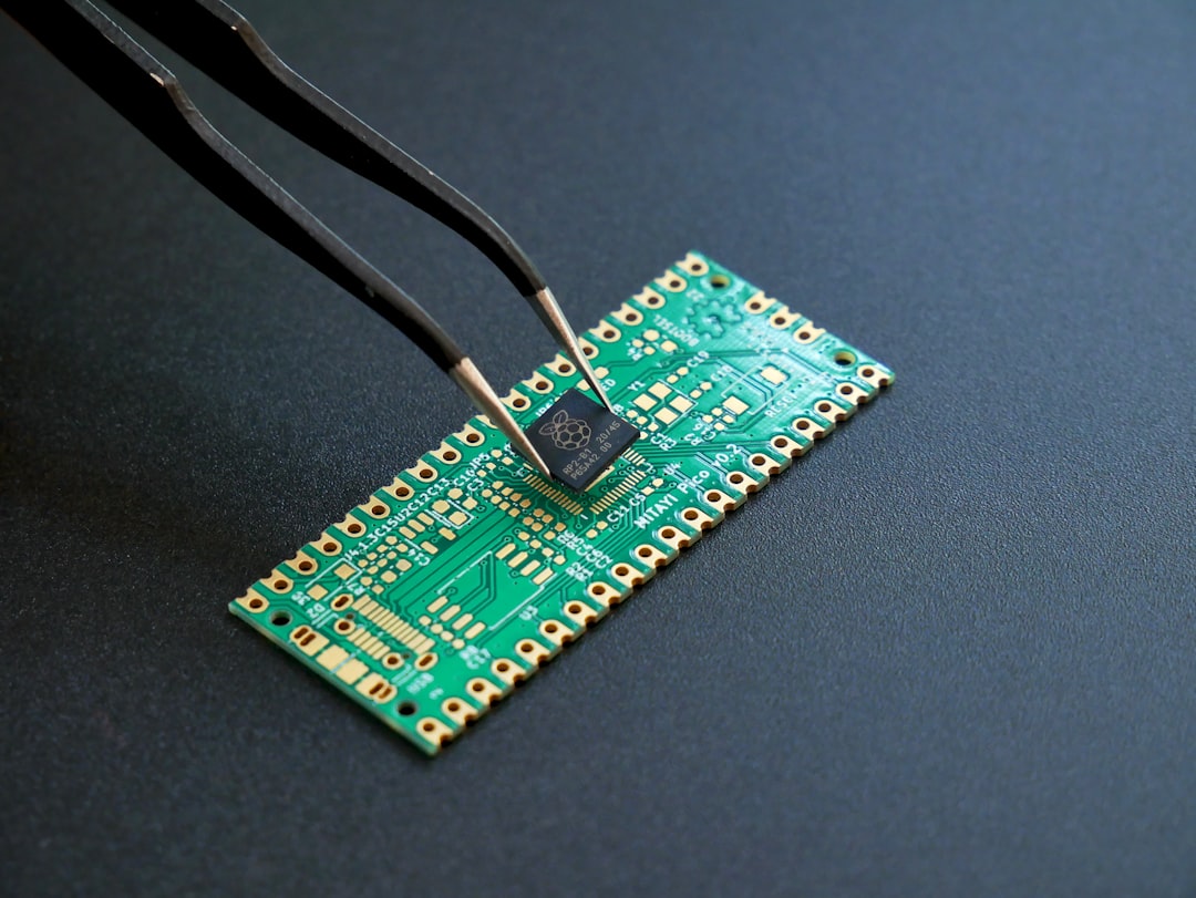 Tweezers placing a small black microchip onto a green circuit board