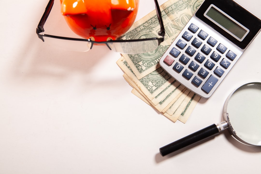 Calculator, magnifying glass, glasses, and money on white surface.